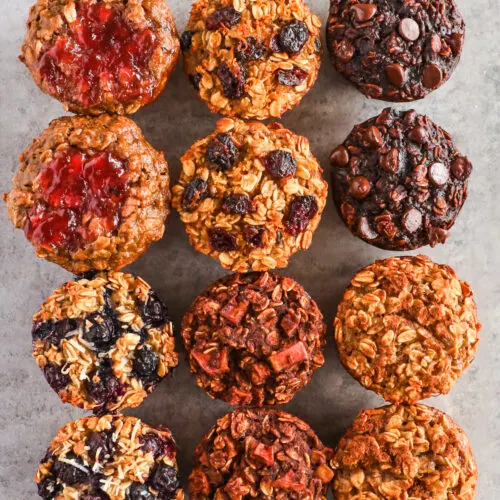 Baked oatmeal cups stacked on table with six flavors including peanut butter & jam, cranberry orange, double chocolate, blueberry coconut, apple cinnamon, and banana bread.