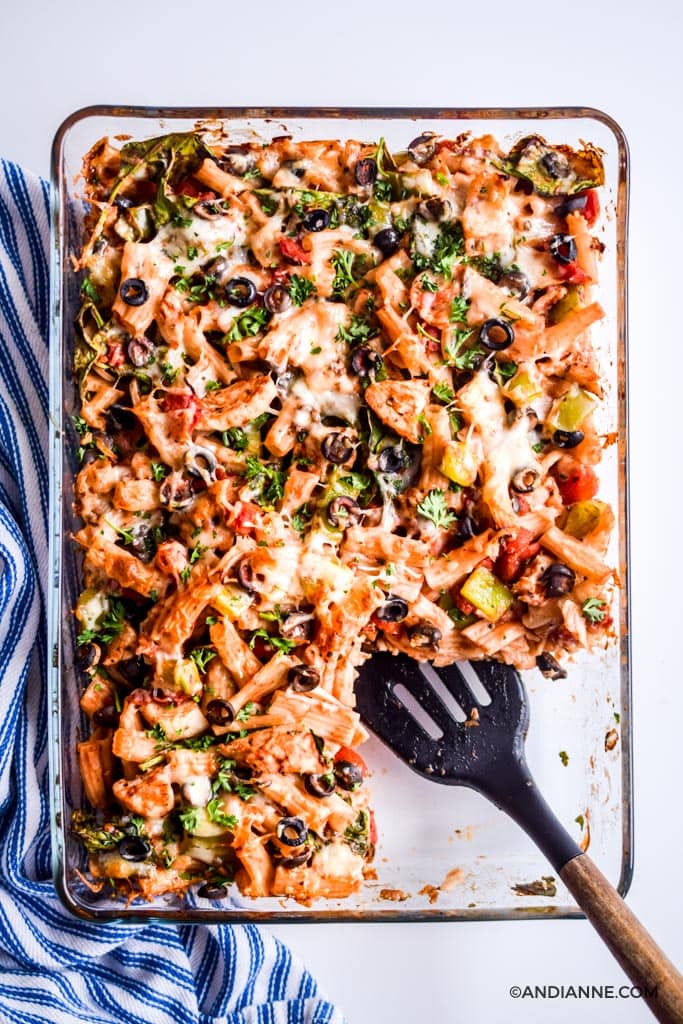 chicken olive pasta bake in glass dish with one slice cut out and a black spatula