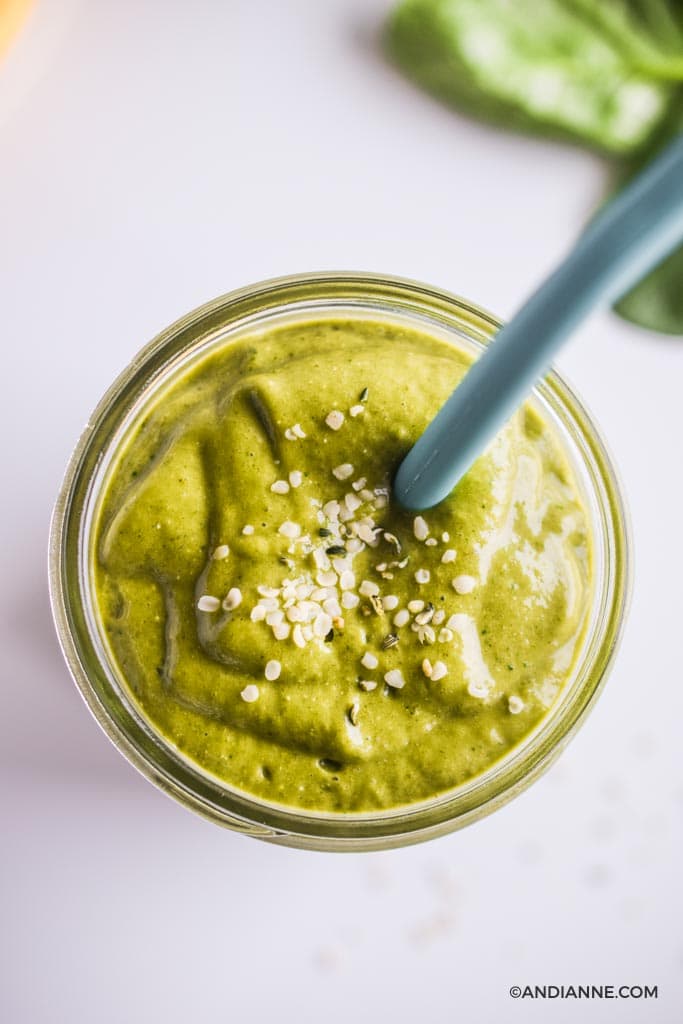 close up detail of green smoothie in glass sprinkled with hemp seeds and has a blue straw