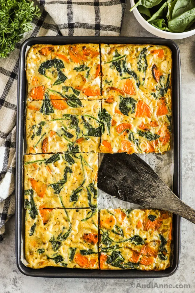 A baking sheet with a sweet potato spinach omelet inside and one slice taken out.