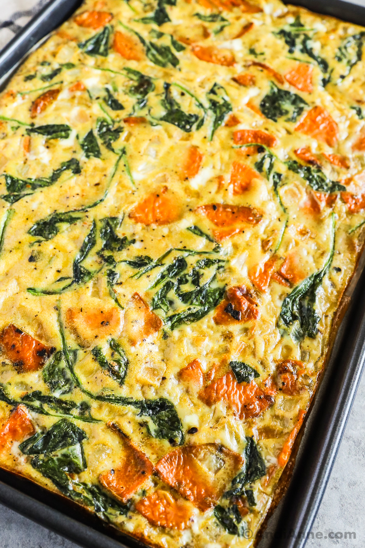 Close up of a large omelette with sweet potato slices and spinach.