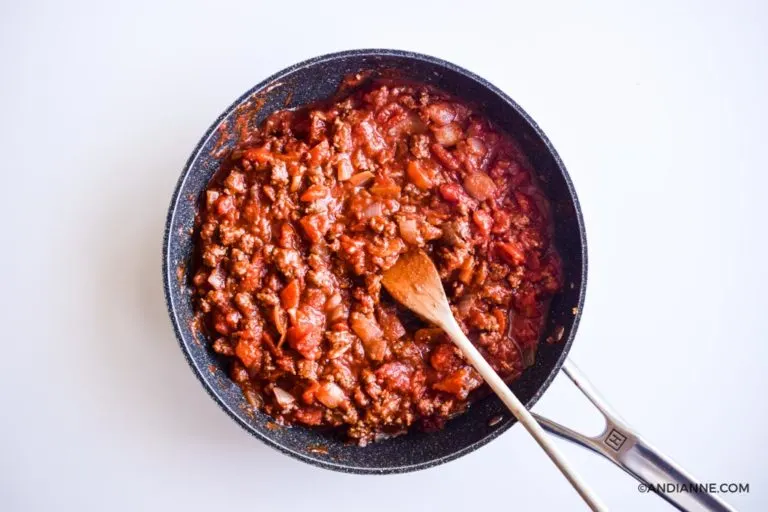 ground beef and tomato sauce in black skillet with wooden spoon