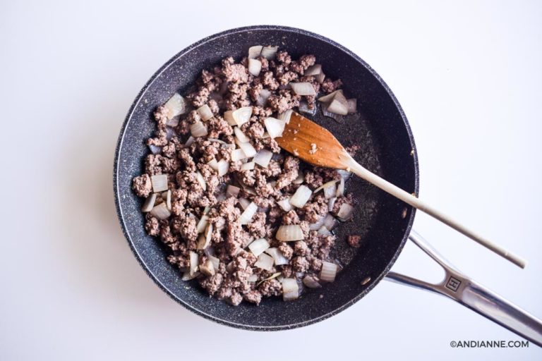 ground beef and chopped onions in a black skillet with wooden spoon