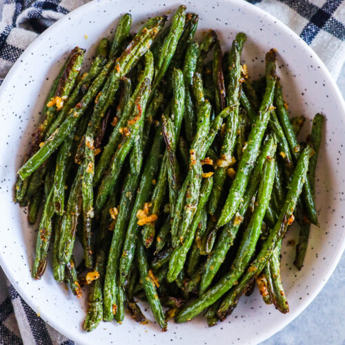 Bowl of crispy green beans with pieces of crispy parmesan cheese pieces.