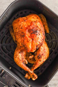 A cooked chicken in an air fryer basket.