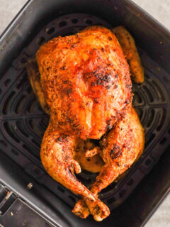 A cooked chicken in an air fryer basket.