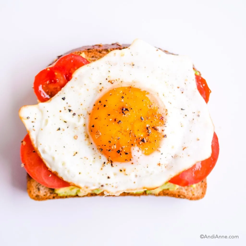 mashed avocado, sliced tomato and fried egg with salt and pepper on piece of toast
