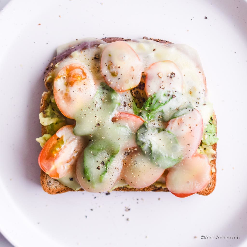 mashed avocado on toast with sliced tomatoes, fresh basil and melted mozzarella cheese