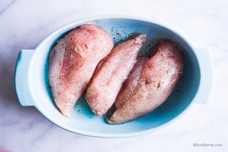 three raw chicken breasts in a blue oval baking dish