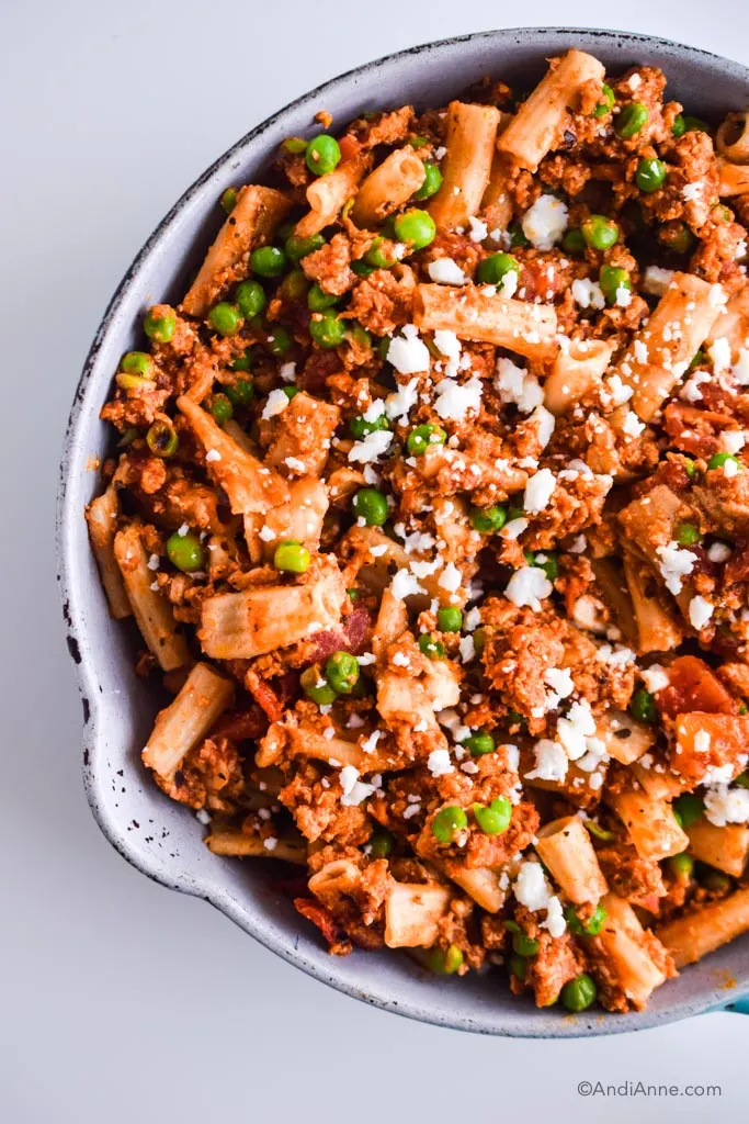 A frying pan with pasta, ground chicken, peas and feta cheese.