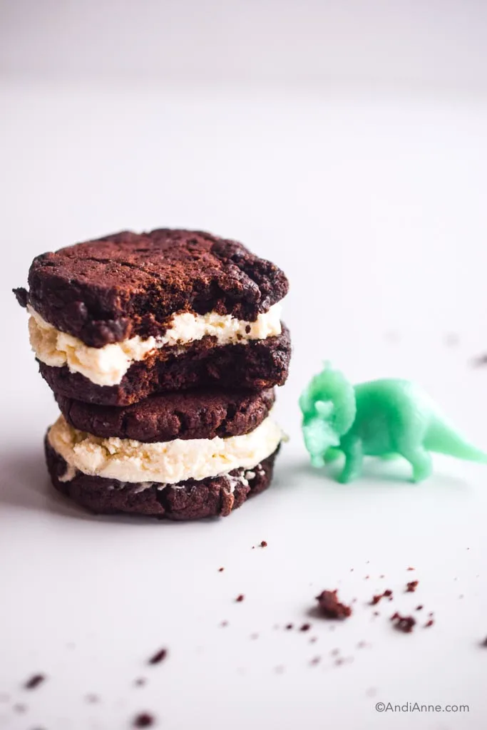 two oreo cookies, one with a bite taken out of it. Green toy dinosaur beside the cookies along with crumbs
