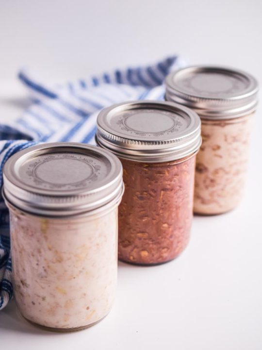 3 sealed mason jars with oats inside them. Blue and white striped napkin behind.