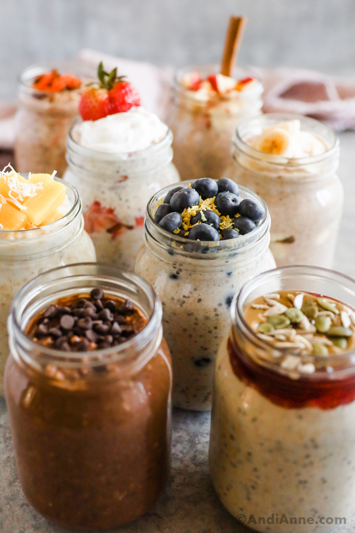 8 different overnight oats flavors in mason jars, all with various toppings including chocolate chips, blueberries, seeds and other fruits. 