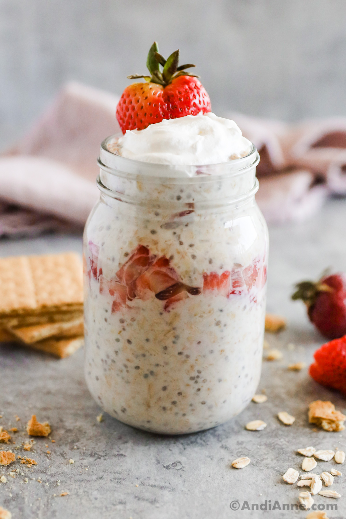 A mason jar with strawberry cheesecake overnight oats, topped with whipped cream and a strawberry.