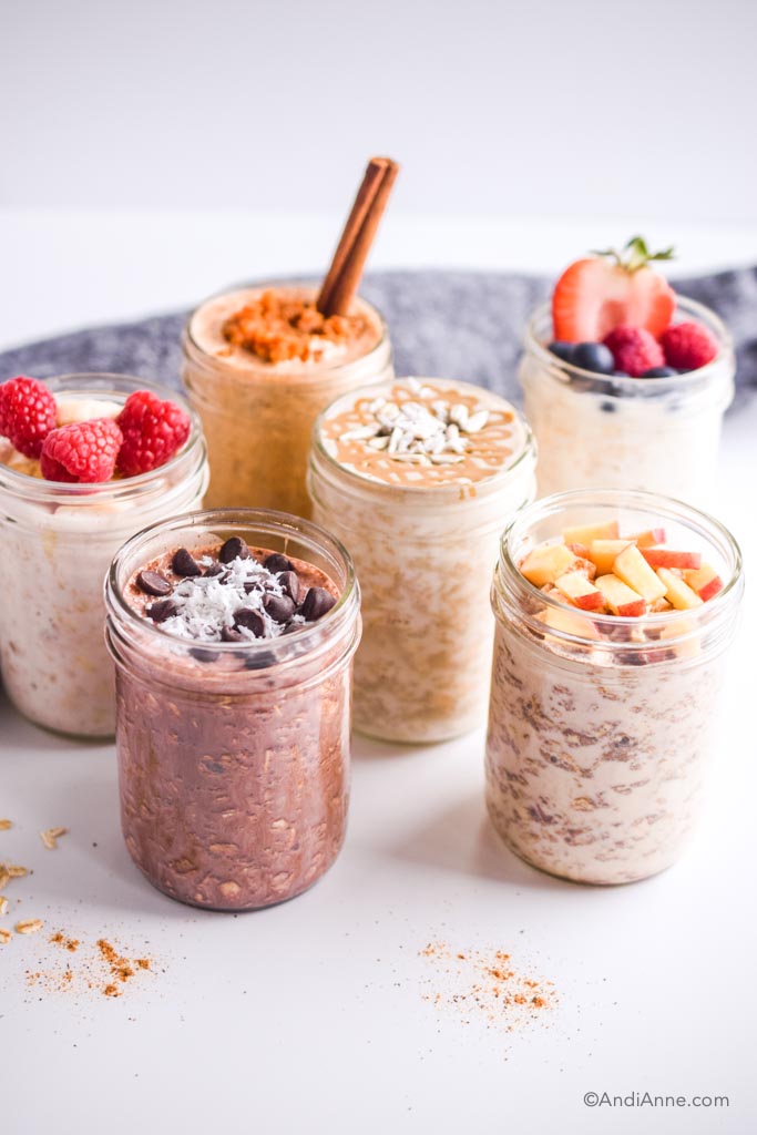 six mason jars with different flavors of overnight oat recipes and fruit toppings.