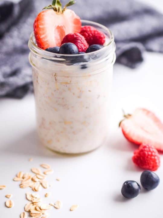 fresh berries on top of oats in mason jar. dark napkin in background