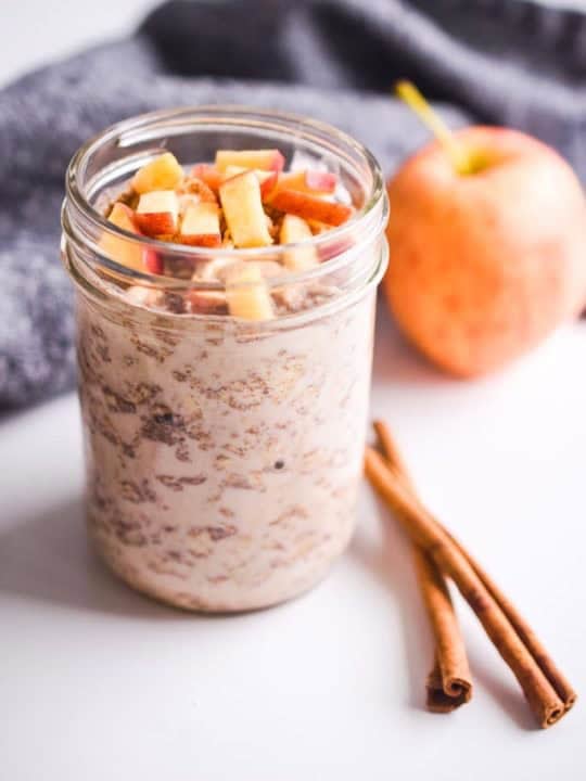 chopped apple on top of apple cinnamon overnight oats. Apple and cinnamon sticks in the background.