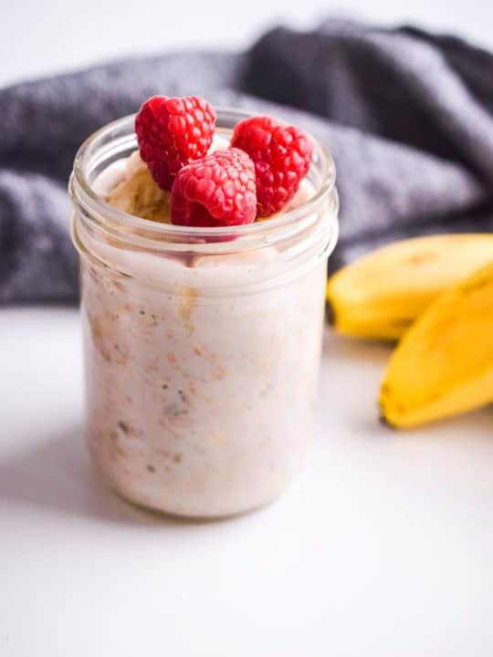 fresh raspberries on top of oats in mason jar. Bananas and dark napkin in background.