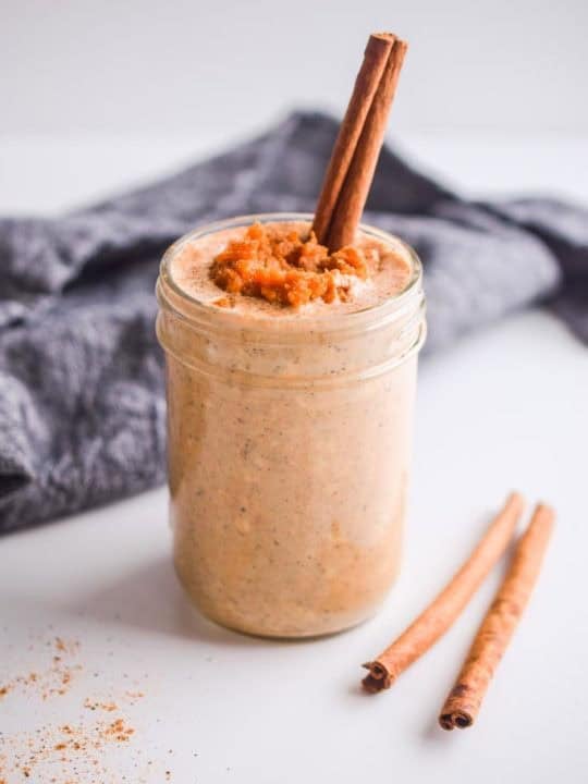 pumpkin pie spice oats in mason jar with cinnamon stick poking in. Two more cinnamon sticks beside the jar and dark napkin behind it.