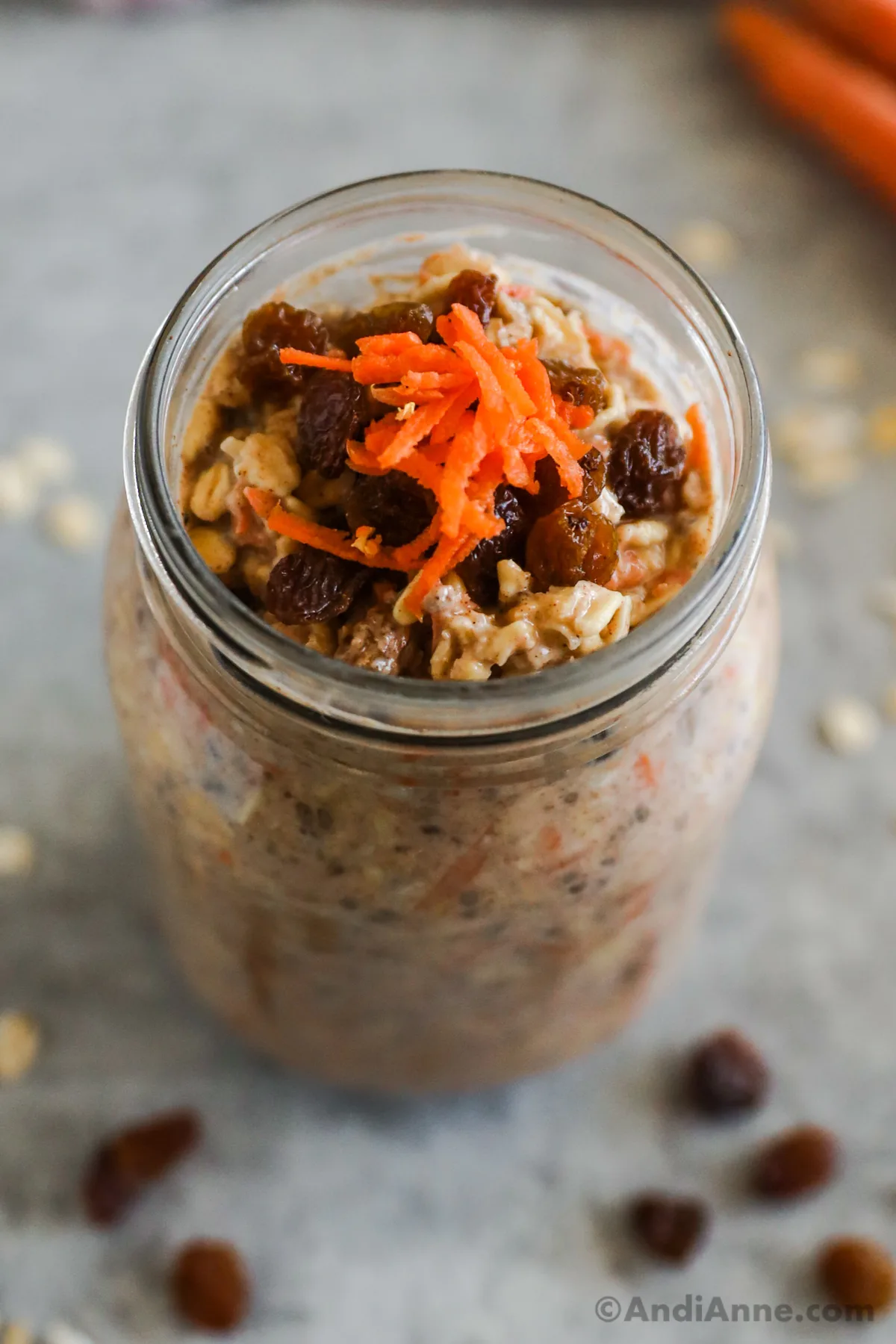 A mason jar with shredded carrot and raisins on top of overnight oats carrot cake flavor.