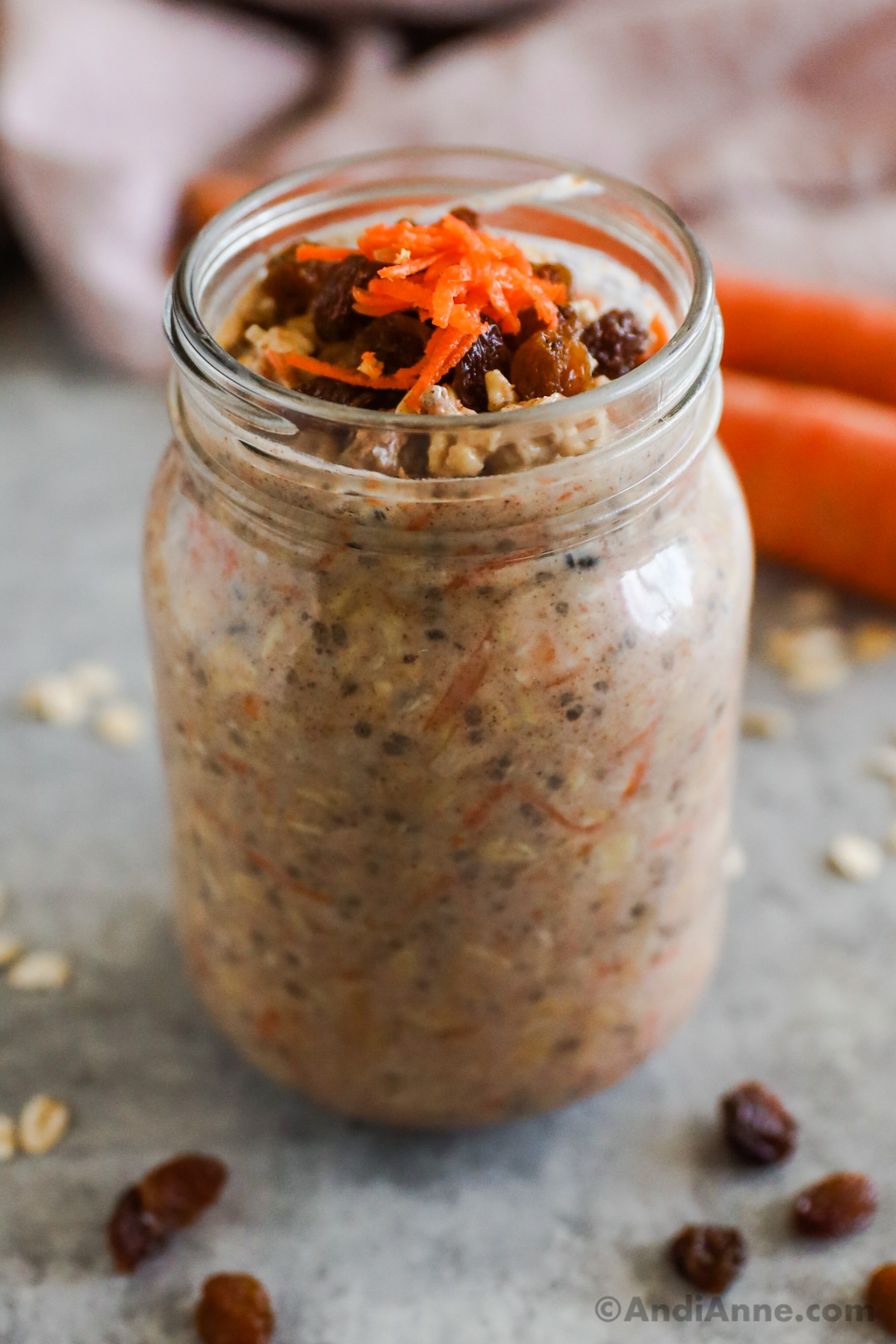 A mason jar with carrot cake overnight oats flavor, topped with raisins and shredded carrots.