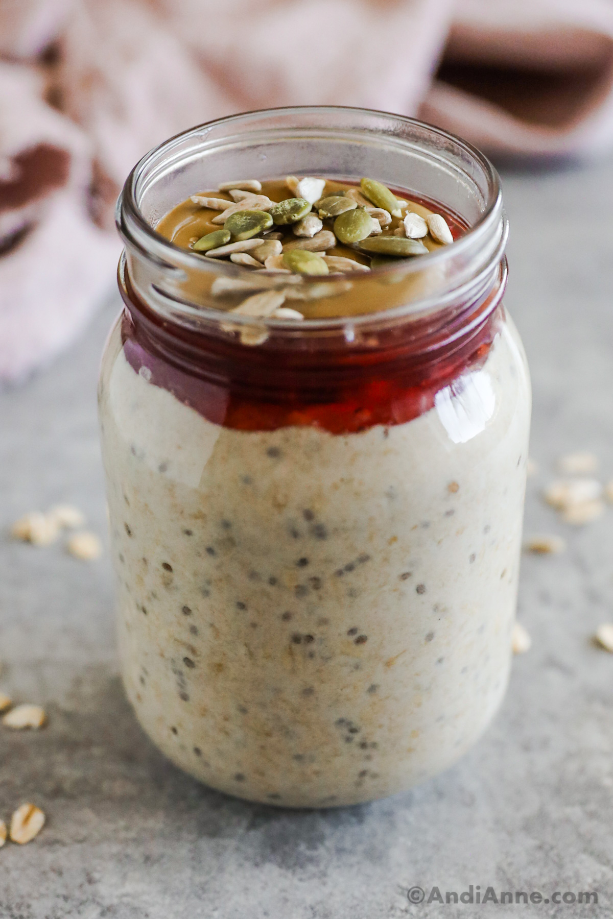 Overnight oats in a mason jar, topped with jam, nut butter and seeds.