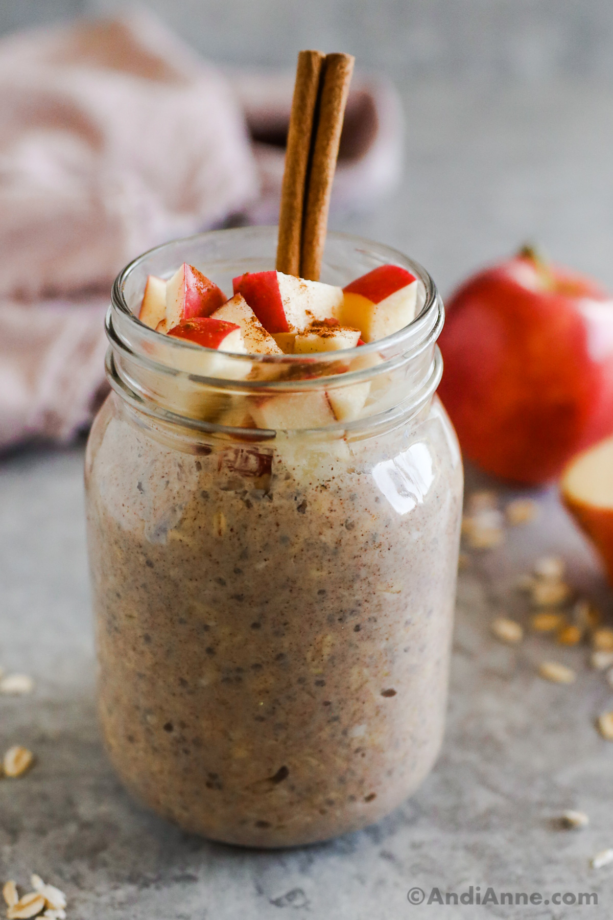 Apple slices overtop of overnight oats in a mason jar with a cinnamon stick poking out the top of the jar.