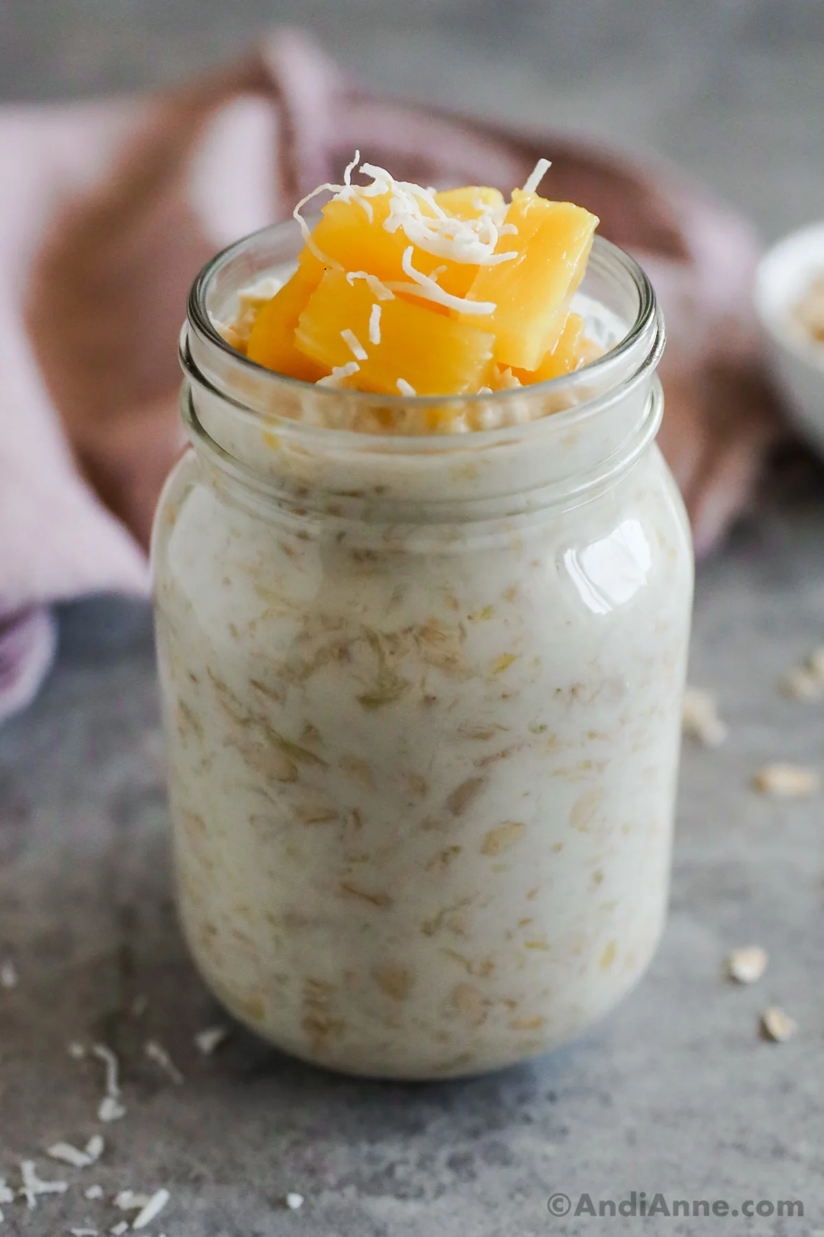Mason jar with overnight oats inside, topped with pineapple and shredded coconut. 