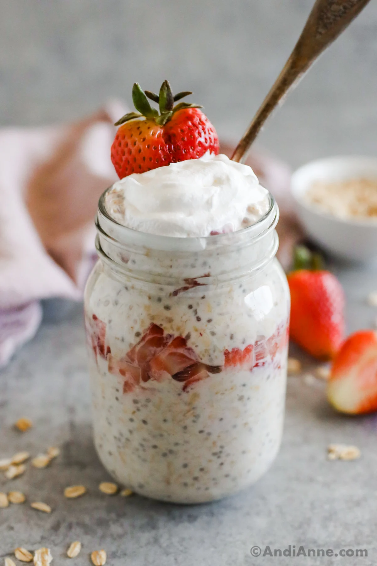 Strawberry cheesecake overnight oats in a mason jar, topped with whipped cream and an extra strawberry.