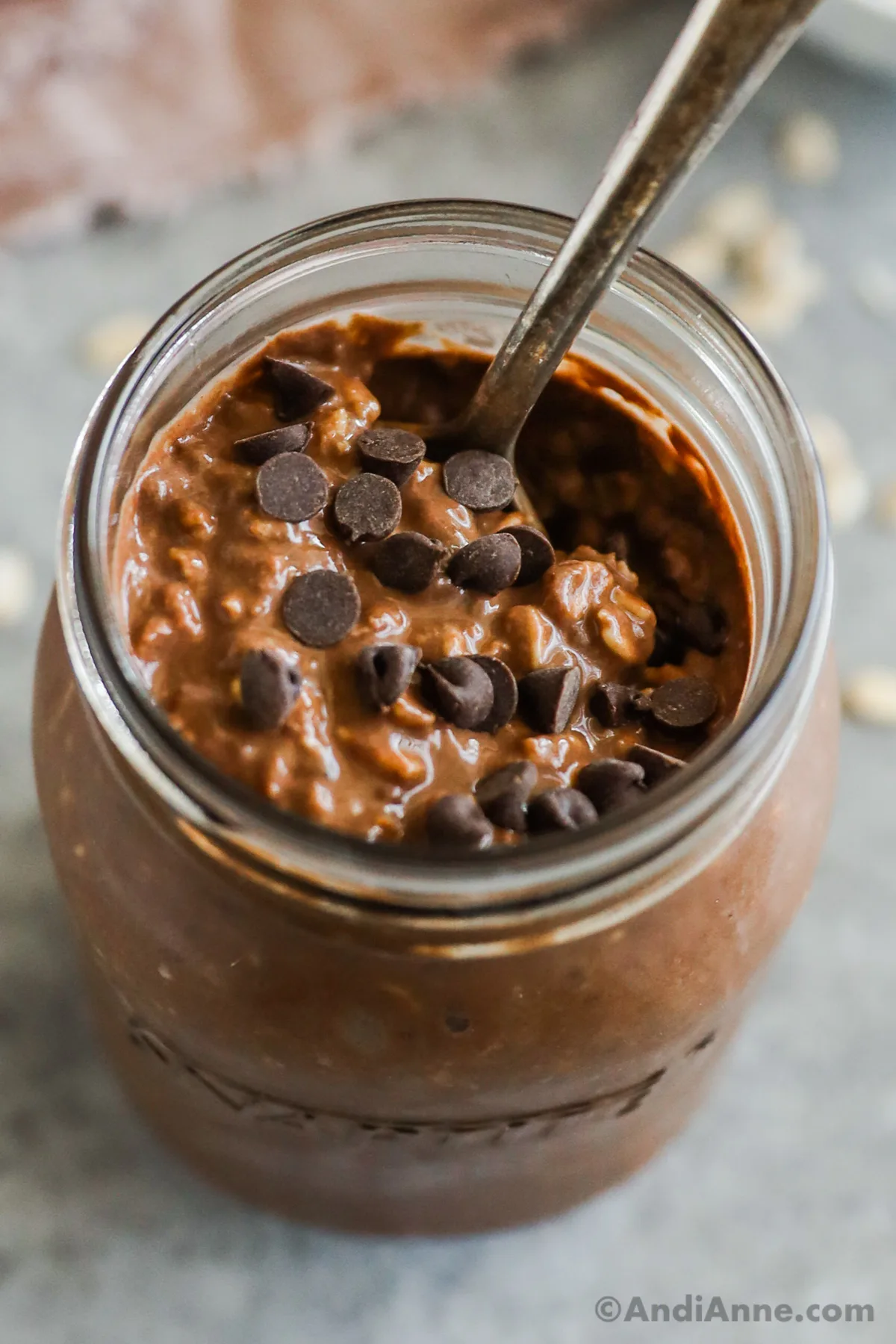 looking down into a mason jar wich chocolate overnight oats inside. Chocolate chips are sprinkled on top and a spoon sits in the jar.
