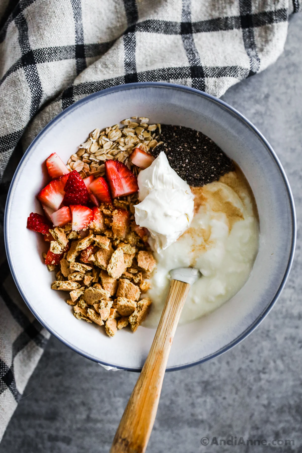 A bowl with crumbled graham cracker, strawberries, yogurt, cream cheese, oats and chia seeds, all unmixed. 