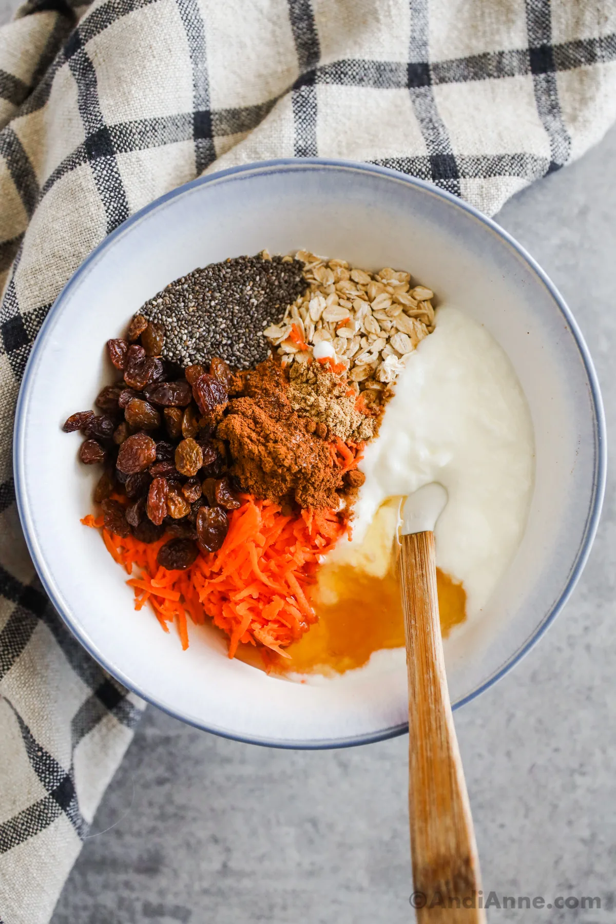 A bowl with yogurt, oats, raisins, shredded carrot, chia seeds and honey. All unmixed.