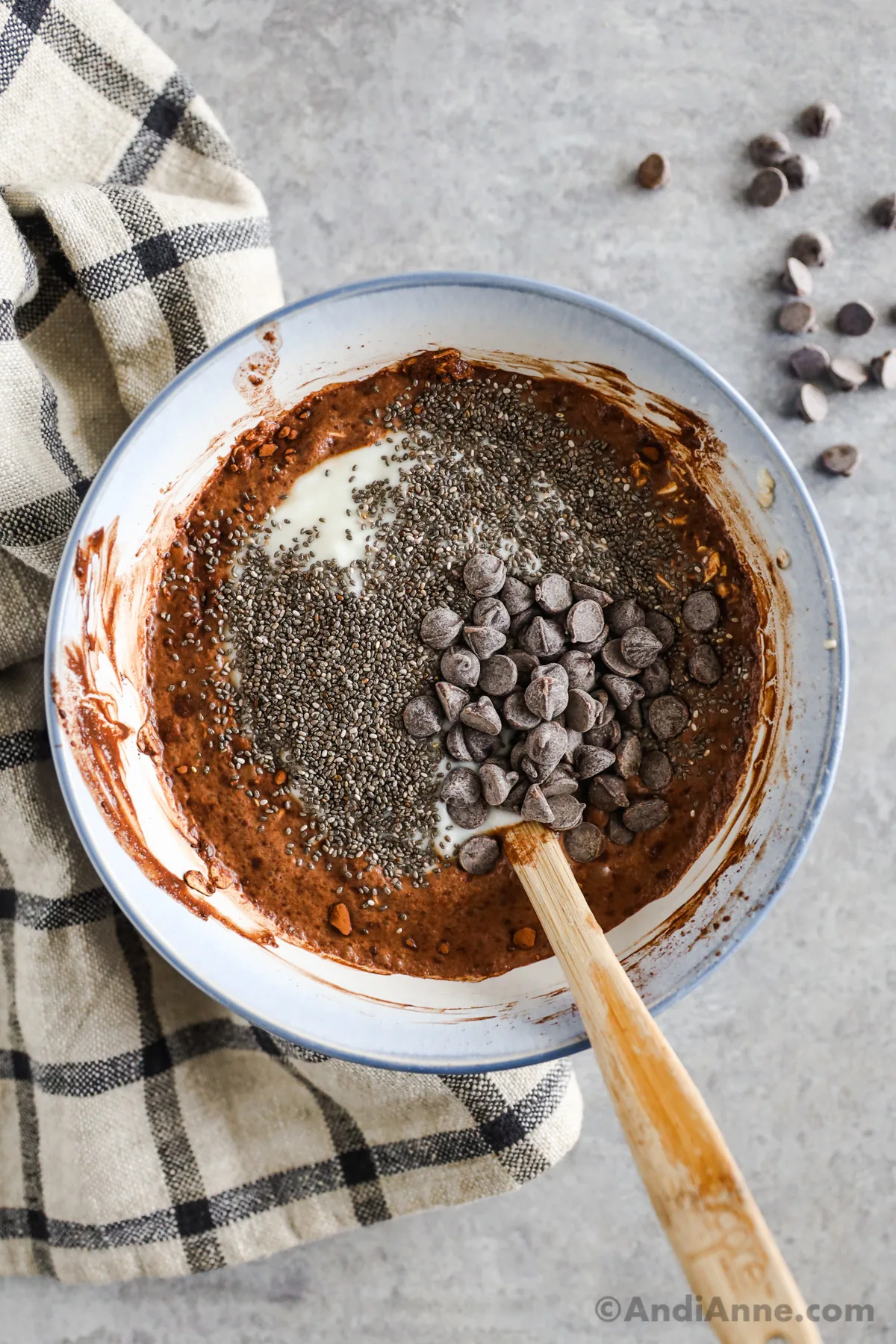 looking down at a bowl with unmixed rolled oats, milk, yogurt, cocoa powder, chocolate chips, honey and chia seeds
