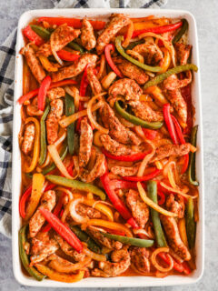 A baking sheet with thin strips of colorful bell pepper, onion and chicken, all covered in a taco seasoning.