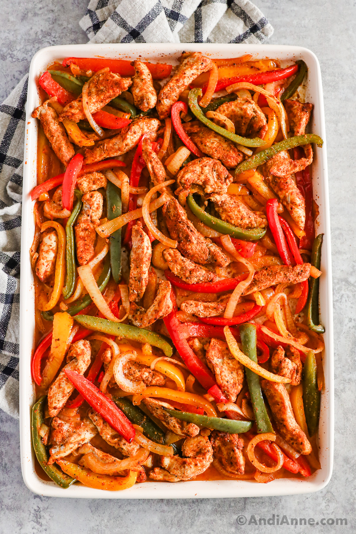 A baking sheet with thin strips of cooked bell pepper, onion and chicken, all covered with taco spices.