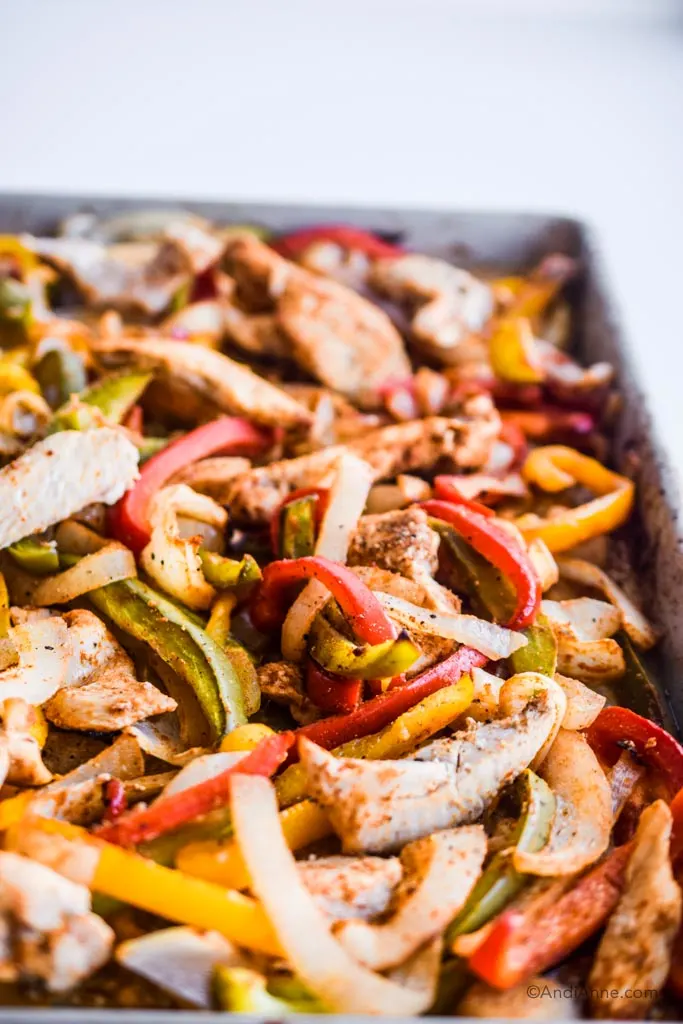 close up detail of chicken, sliced onion, sliced red, green and yellow bell peppers in a sheet pan