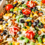 a tray of ground beef sheet pan nachos with tomatoes, olives and melted cheese