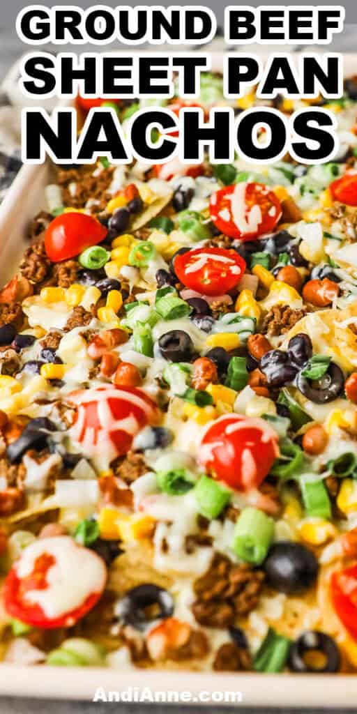 a tray of ground beef sheet pan nachos with tomatoes, olives and melted cheese