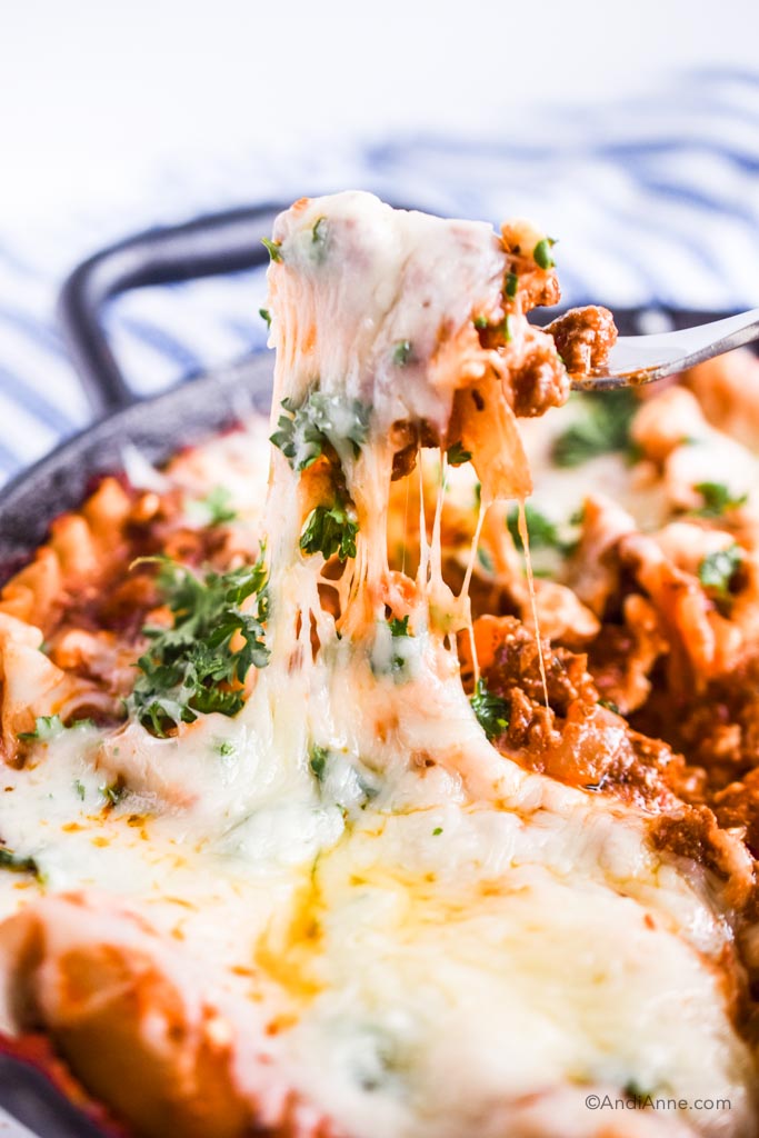 Fork pulling up melted cheese from a lasagna in a skillet