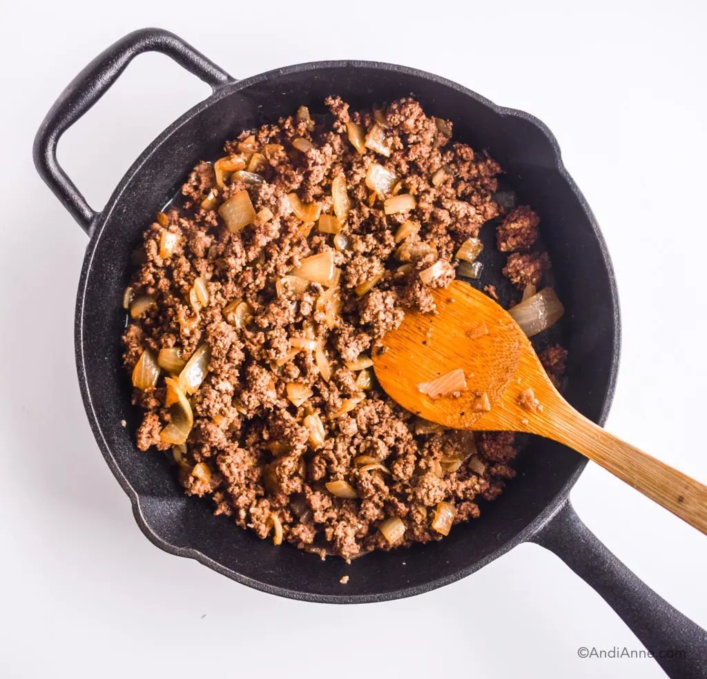 ground beef with onions in a black skillet with wooden spoon