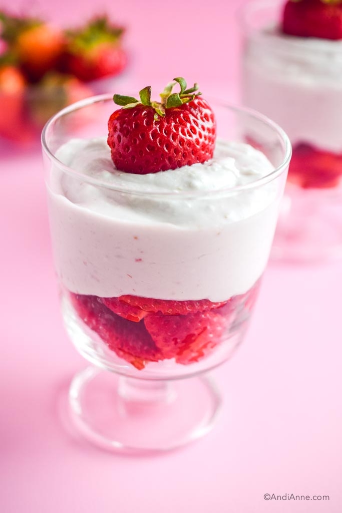 strawberries and cream in dessert glass with pink background and extra bowl of strawberries
