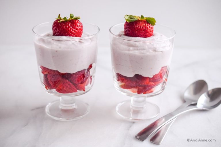 two strawberries and cream desserts with two spoons beside them