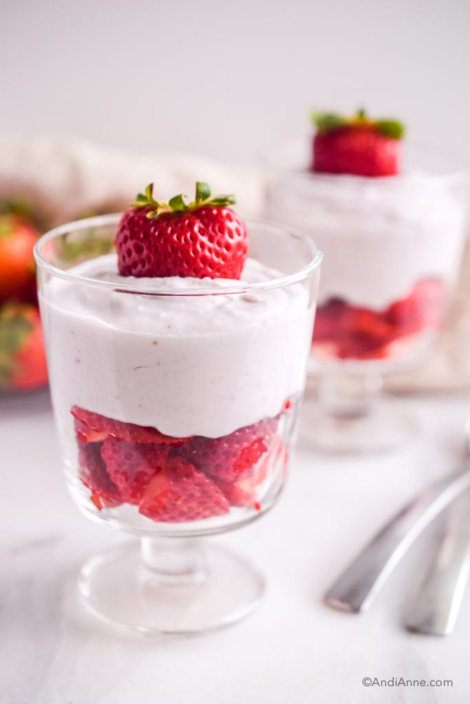 strawberries and cream in a glass cup with spoons in the background