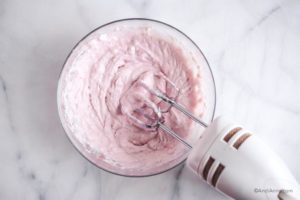 blending pink coconut cream with a white electric mixer in a glass bowl