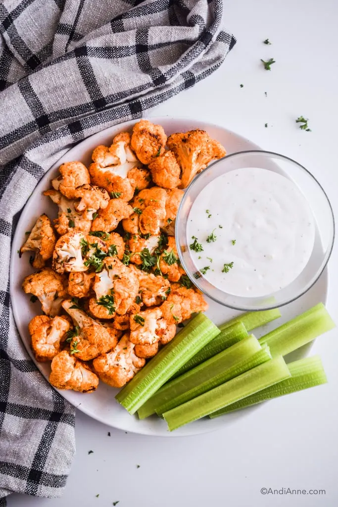 air fryer buffalo cauliflower bites on a white plate with ranch dip and celery sticks