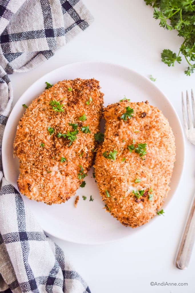 crispy air fryer parmesan chicken breasts on a white plate with napkin and forks beside it