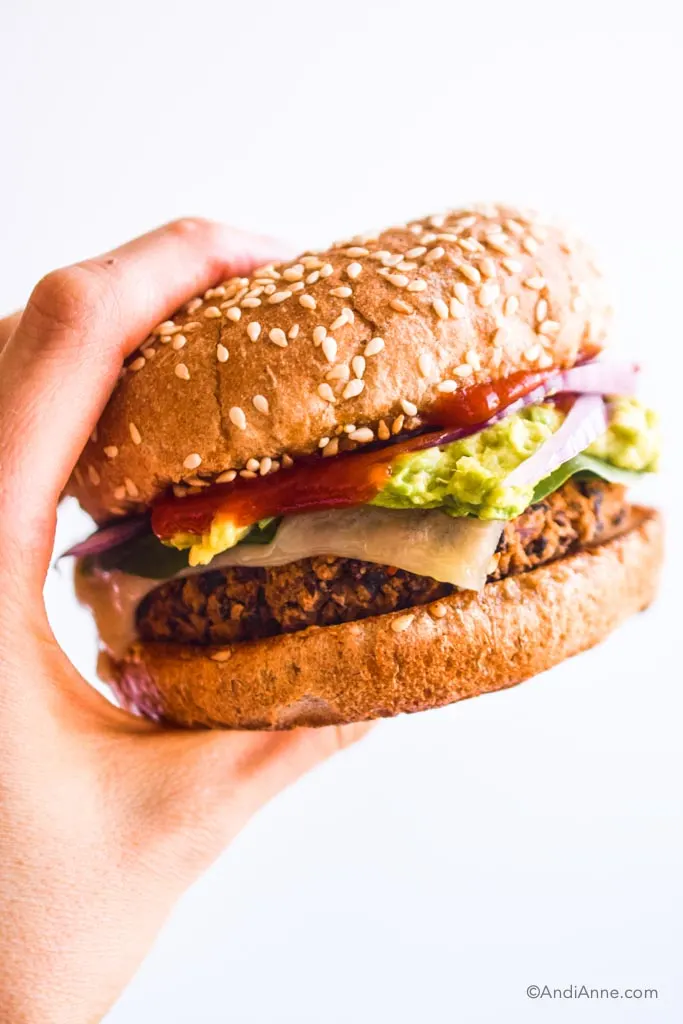hand holding a black bean burger with ketchup, avocado, sliced onion and melted cheese