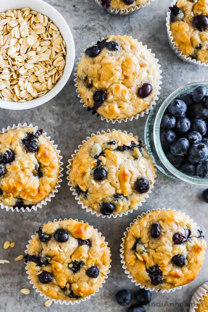 Blueberry muffins on a counter with a bowl of rolled oats and fresh blueberries.