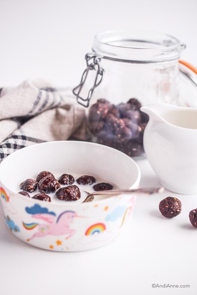 kids unicorn bowl with milk and homemade chocolate cereal. Glass jar with more chocolate cereal and milk container in background