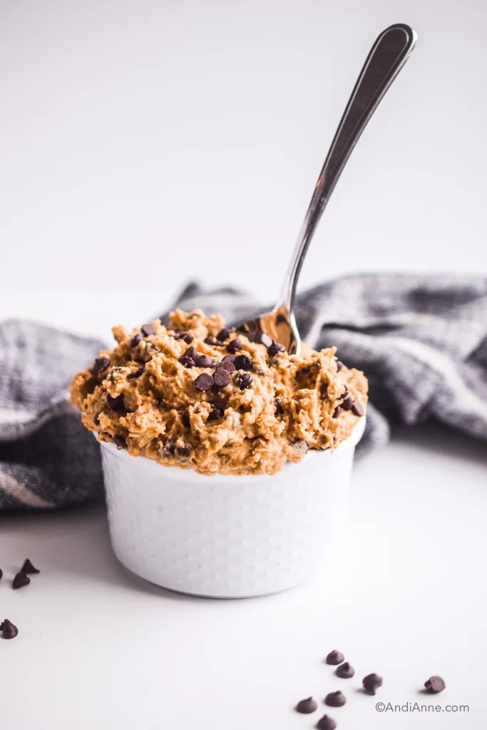 small white bowl of cookie dough mixture and spoon stuck in it. Black napkin behind. 